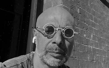 A man in a black-and-white portrait, wearing round glasses